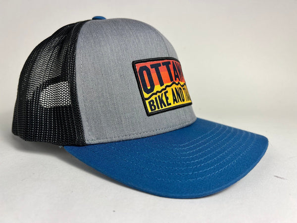 Ottawa Bike and Trail, LLC Shop Merch Black Light Blue OBAT Logo Sunrise Trucker Hat